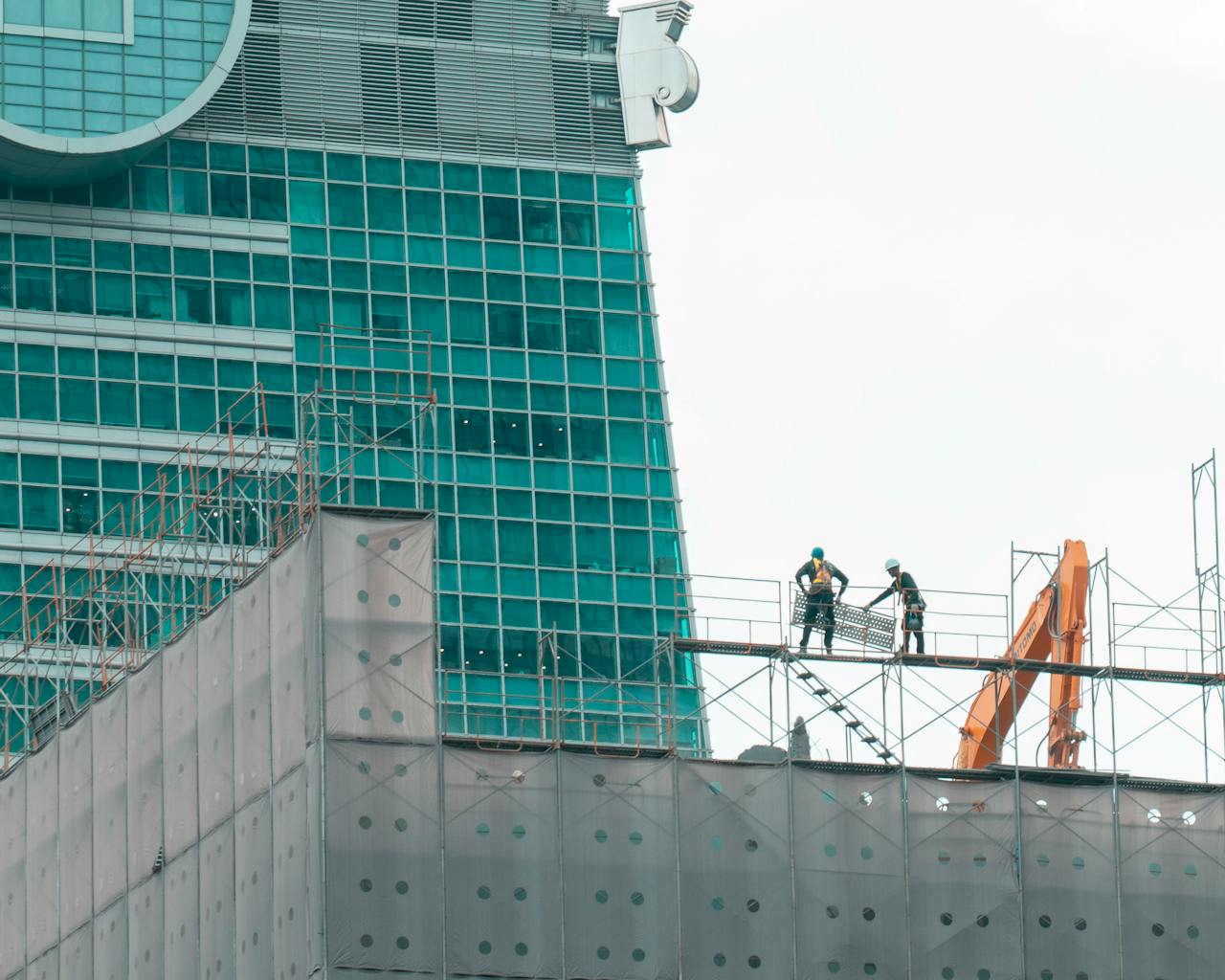 why-choose-us Two construction workers on scaffolding in front of a modern skyscraper under construction.