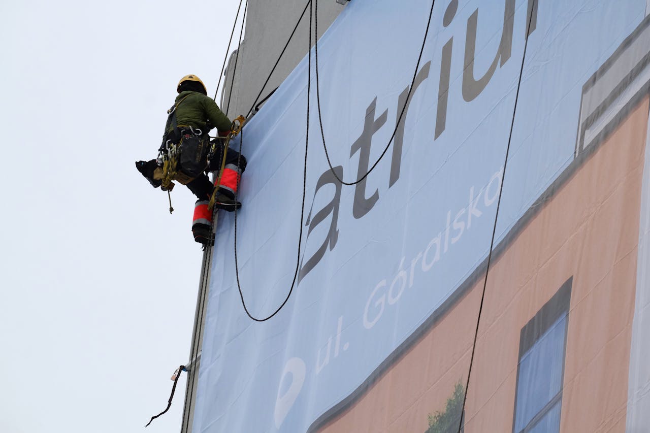services-03 A worker on ropes installs a large banner on a building exterior.